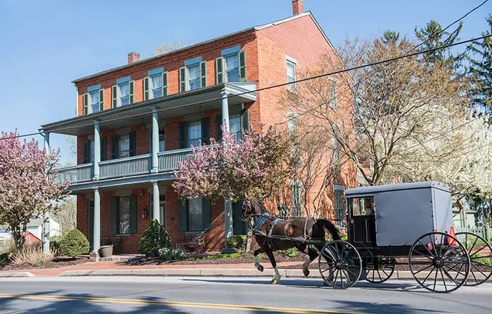 An exterior view of Bird in Hand, PA's historical AmishView Inn and Suites as a Amish horse-drawn buggy rides by.